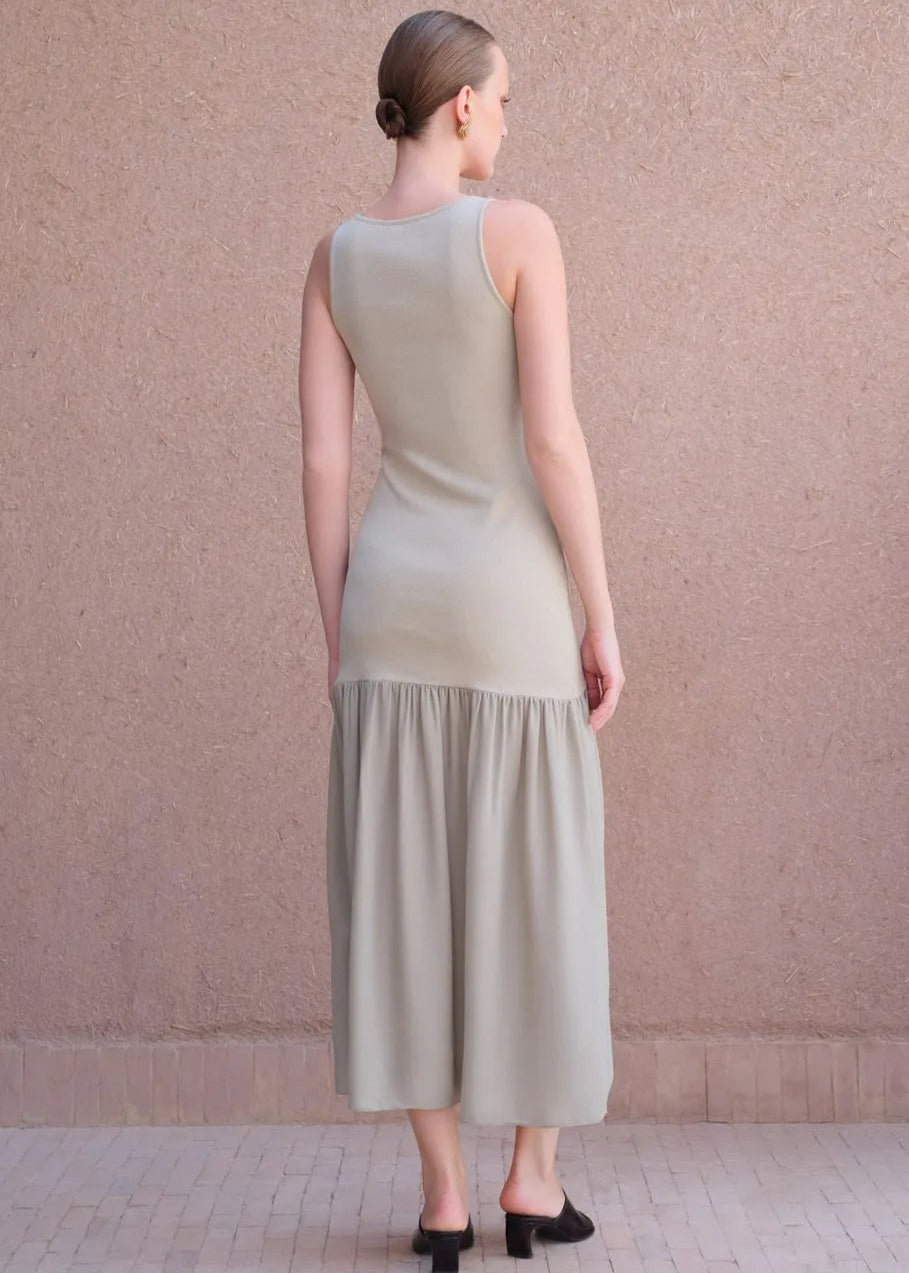 Woman wearing a light green dress standing against a beige wall.