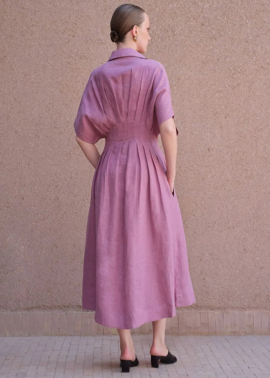 Woman wearing a purple dress standing against a beige wall.