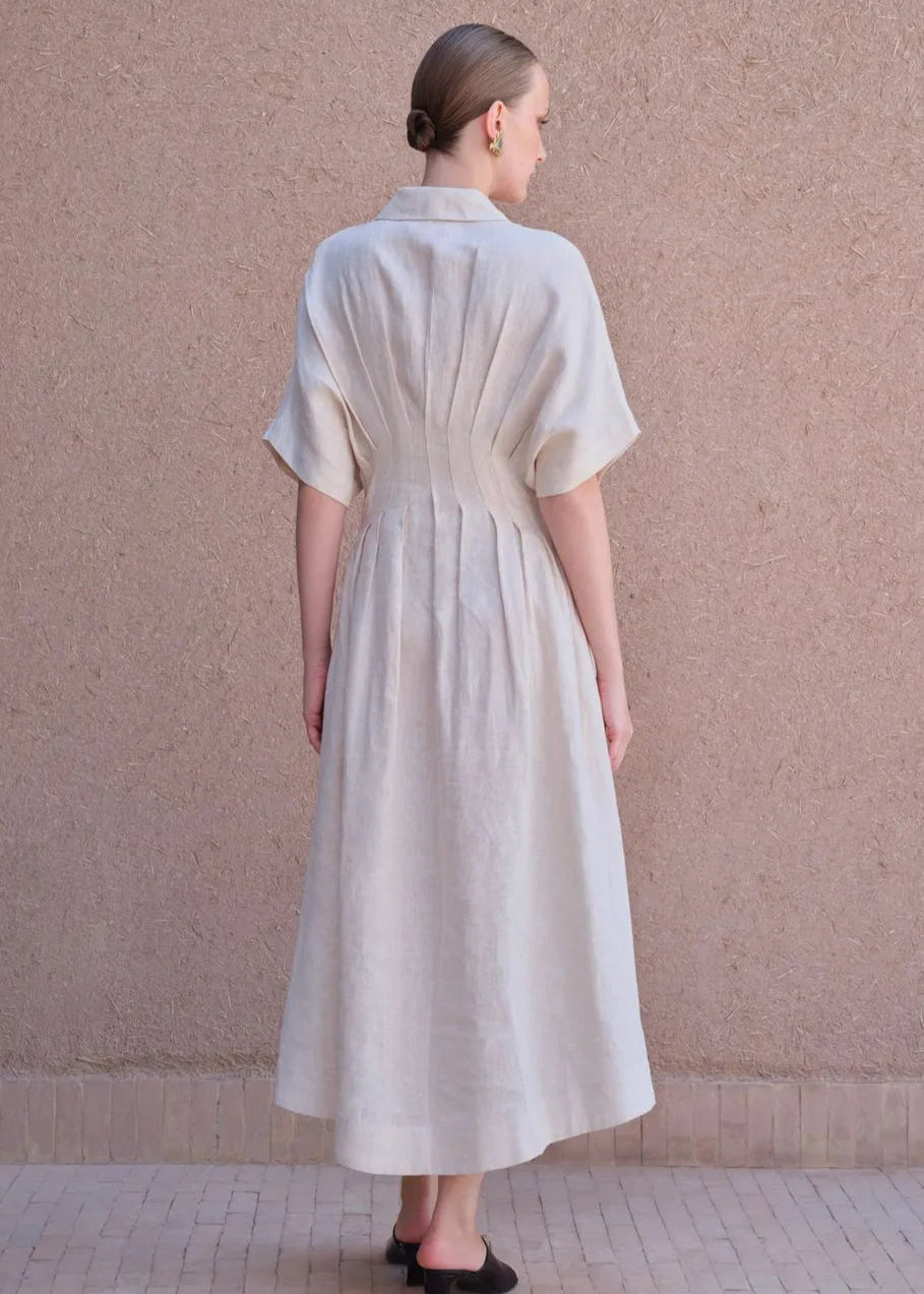 Woman wearing a long, light-colored dress against a beige wall.