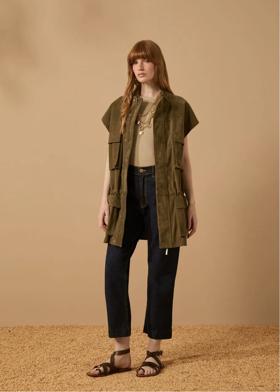 Woman wearing an olive green vest over a beige top and dark pants on a beige background