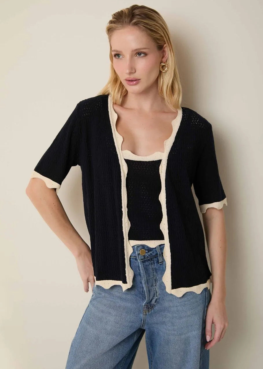 Woman wearing a black cardigan with white trim and blue jeans against a plain background