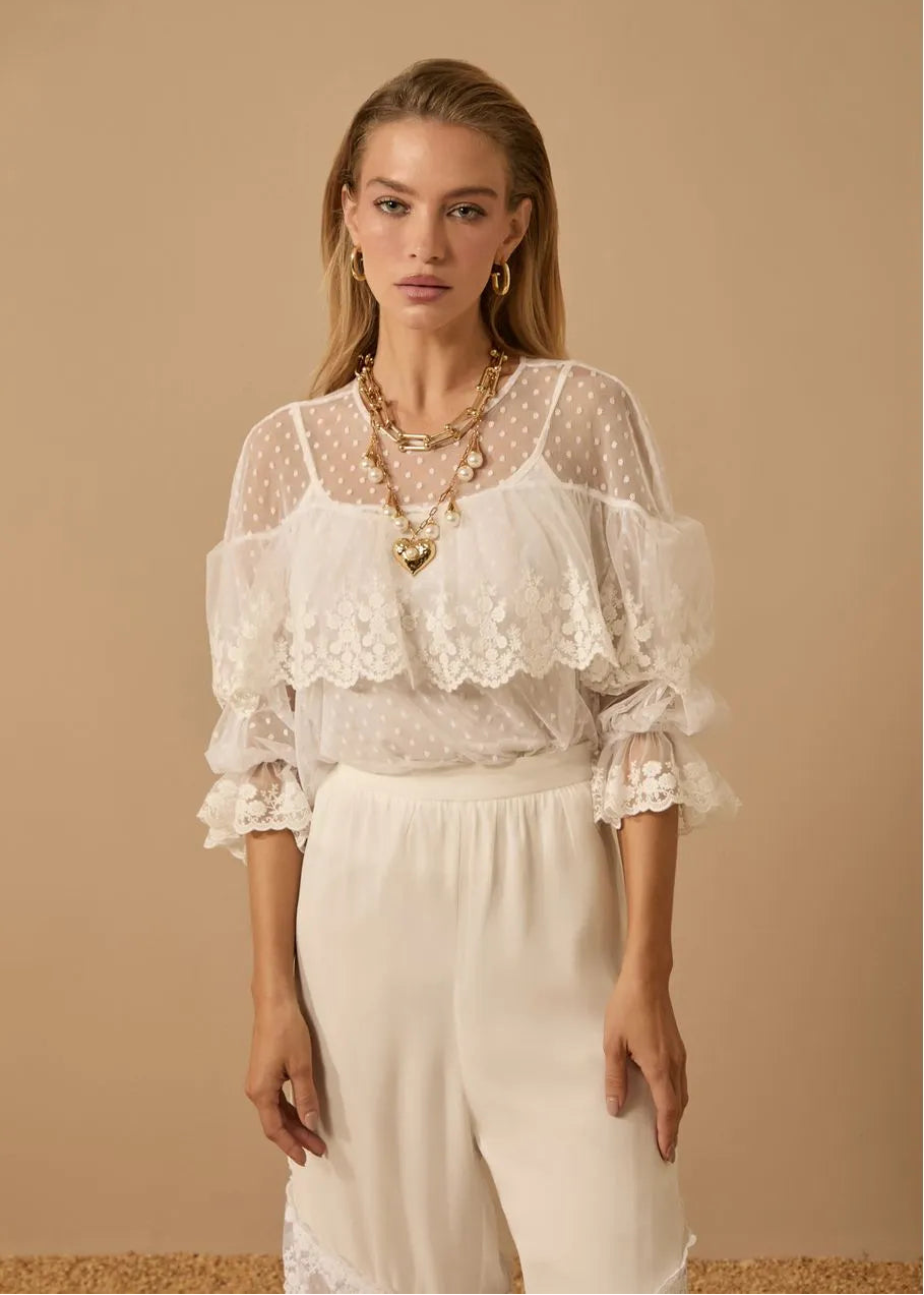 Woman wearing a white lace blouse and white pants against a beige background