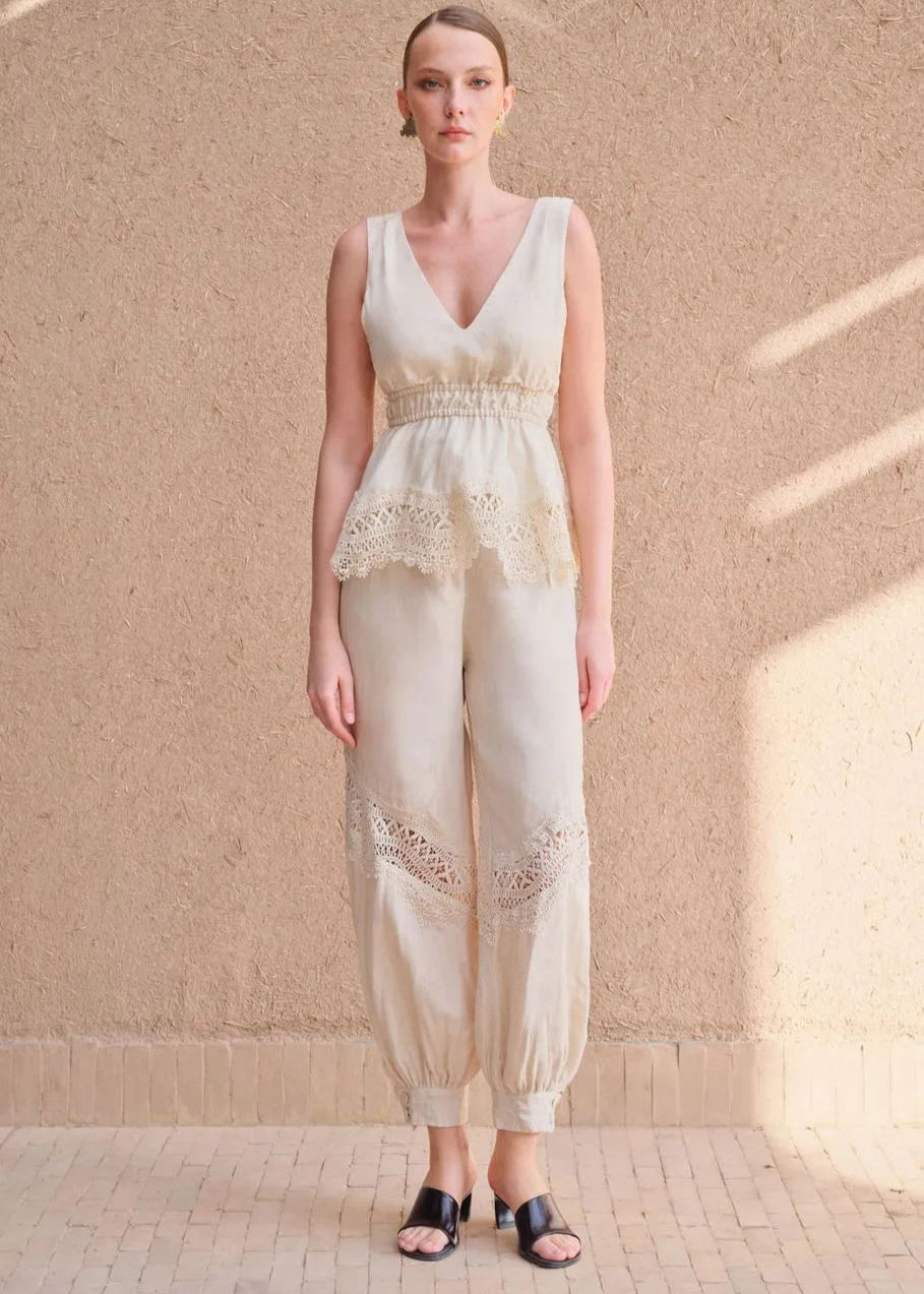Woman wearing a white lace jumpsuit against a beige wall.