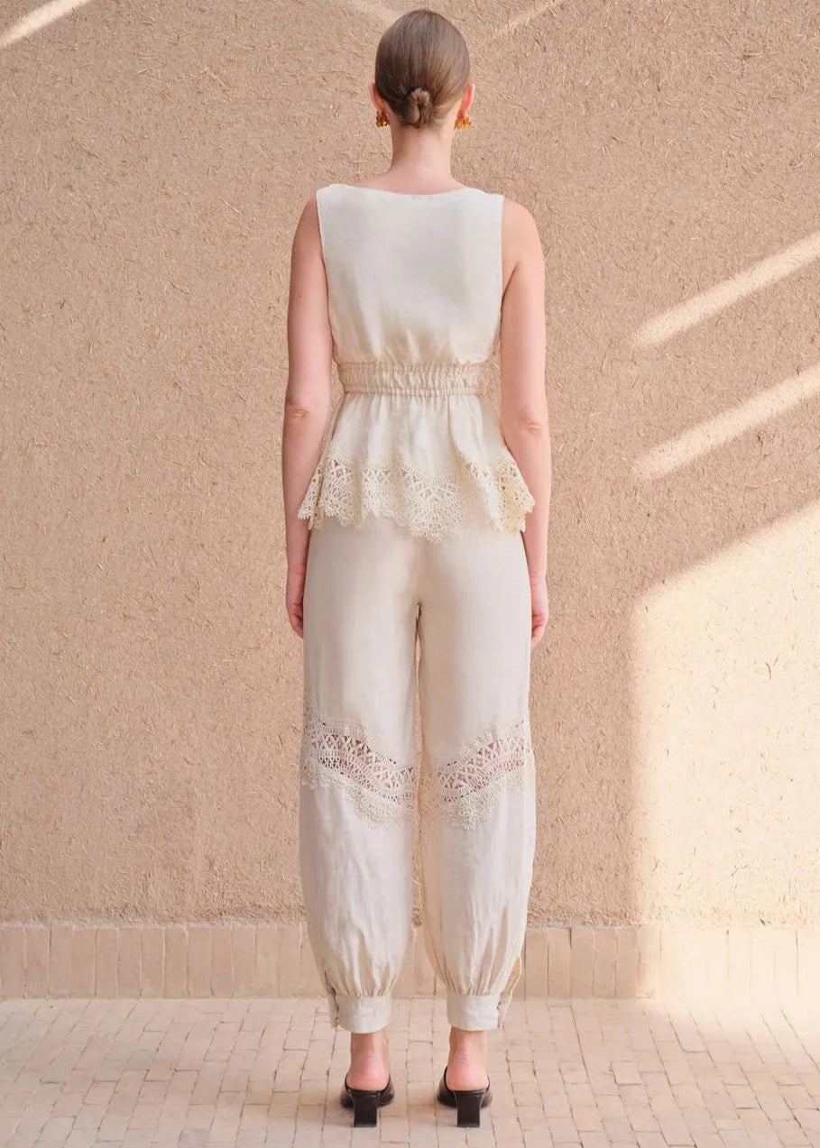 Woman wearing a white lace jumpsuit standing against a beige wall.