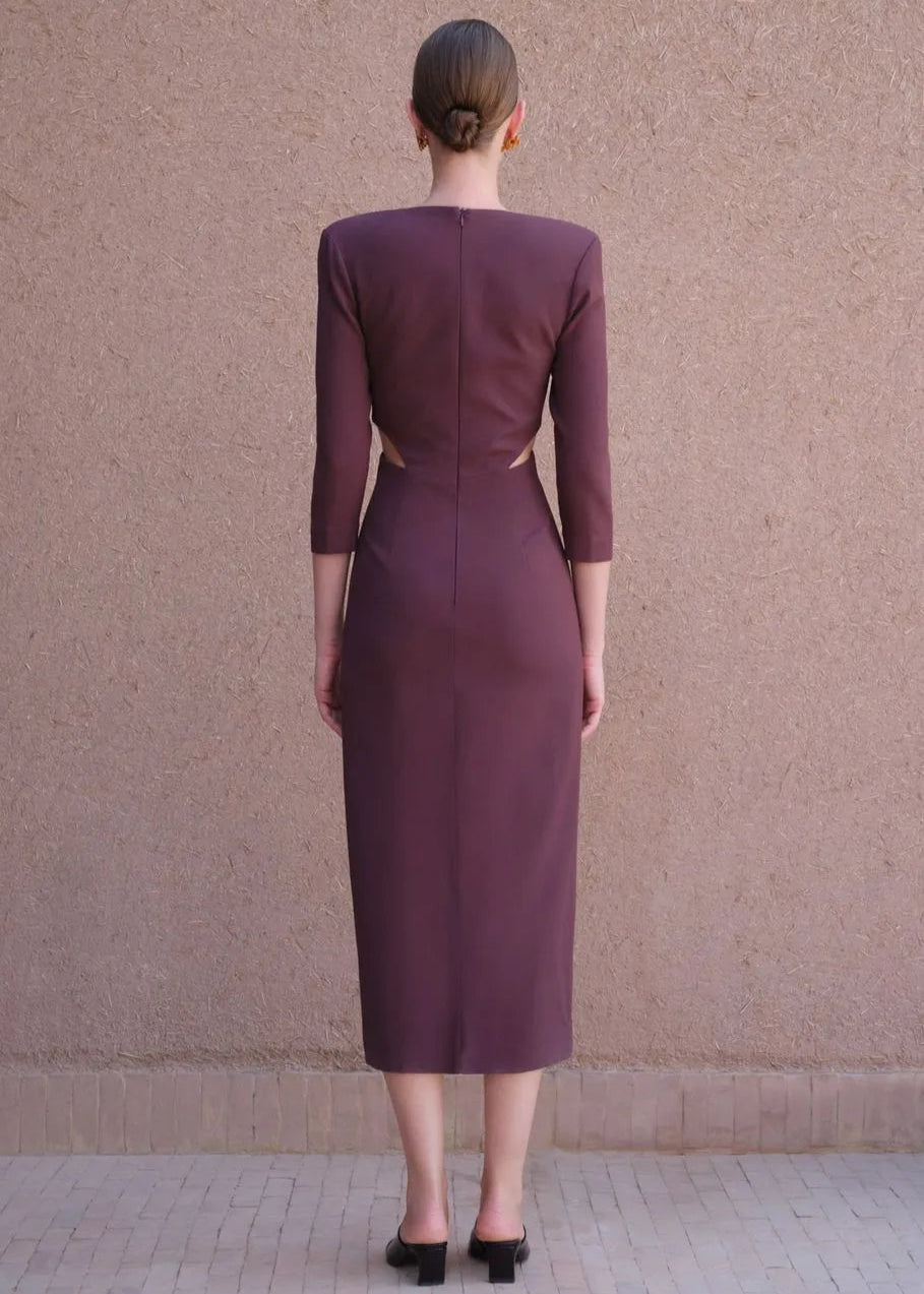 Woman wearing a burgundy dress with cut-out design on a plain background