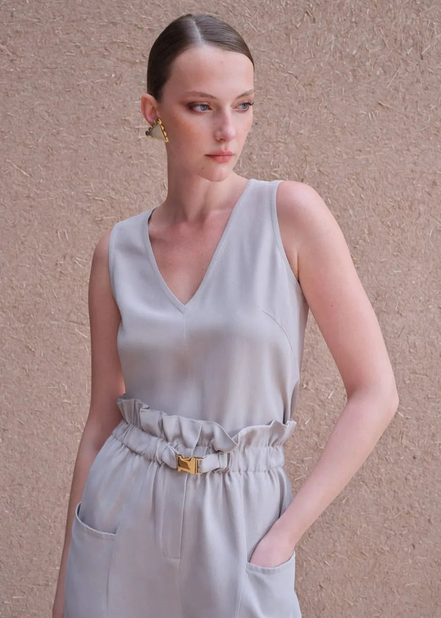 Woman wearing a light gray sleeveless jumpsuit against a beige background
