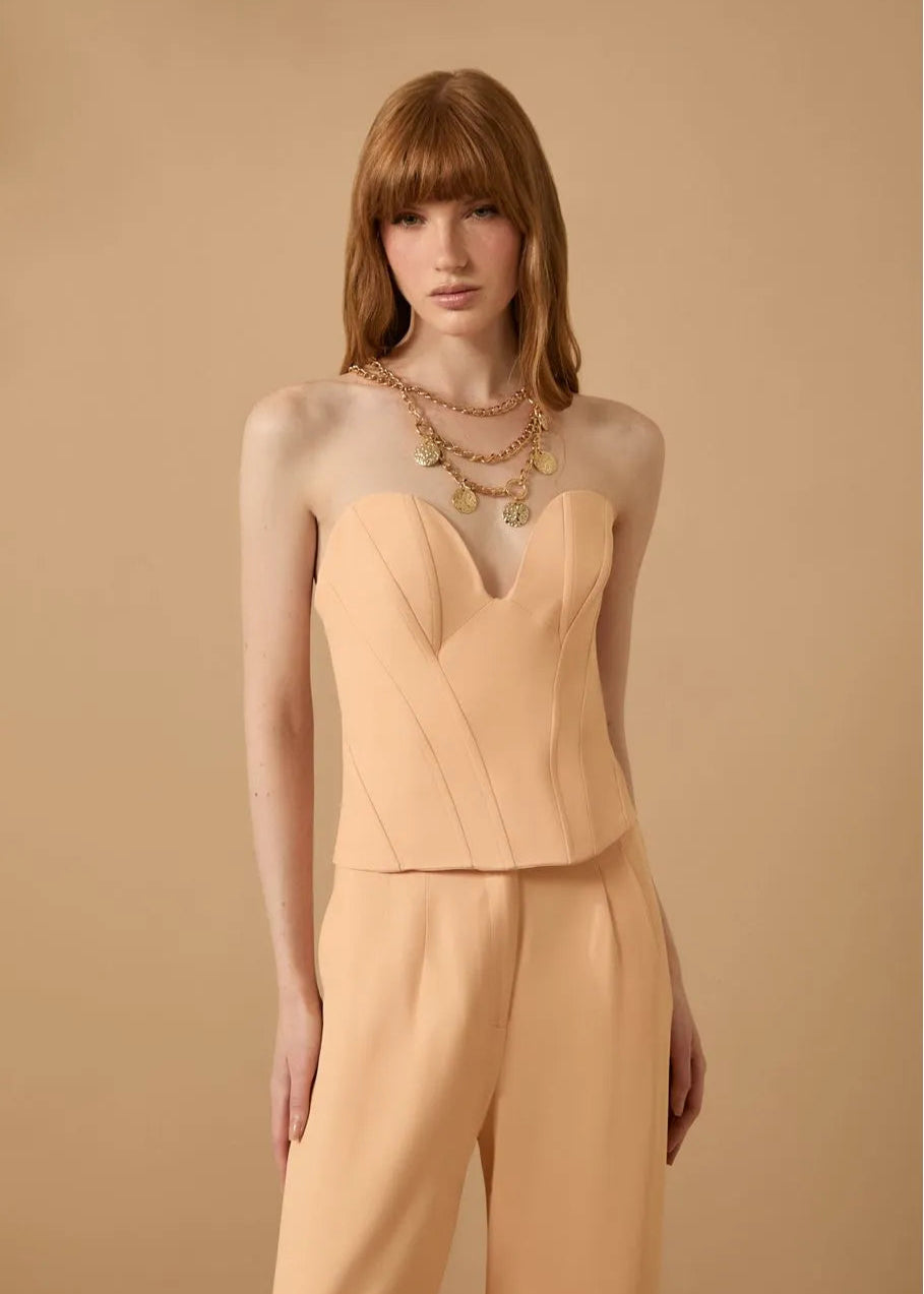 Woman wearing a beige top and pants with layered necklaces against a beige background