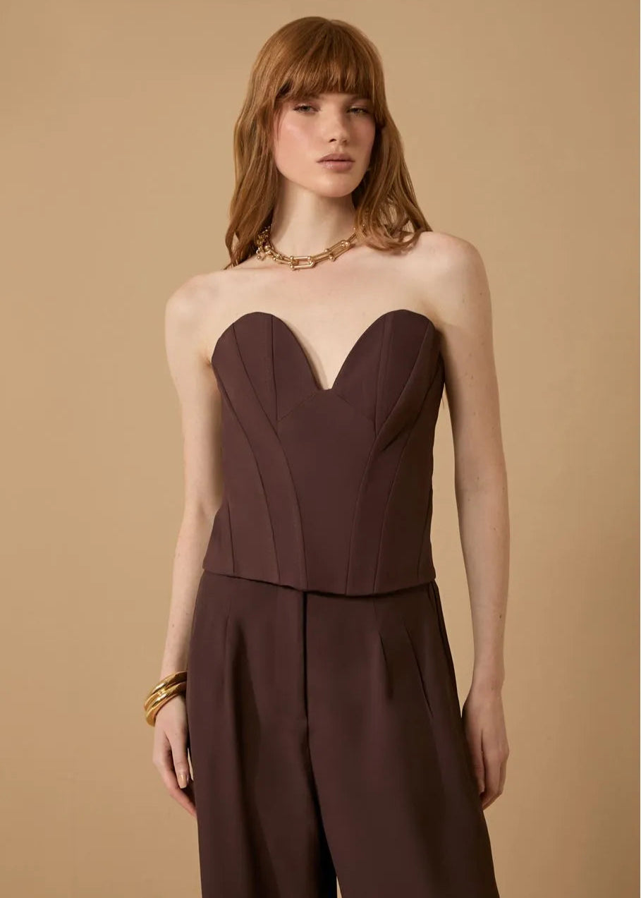 Woman wearing a brown strapless top and pants against a beige background