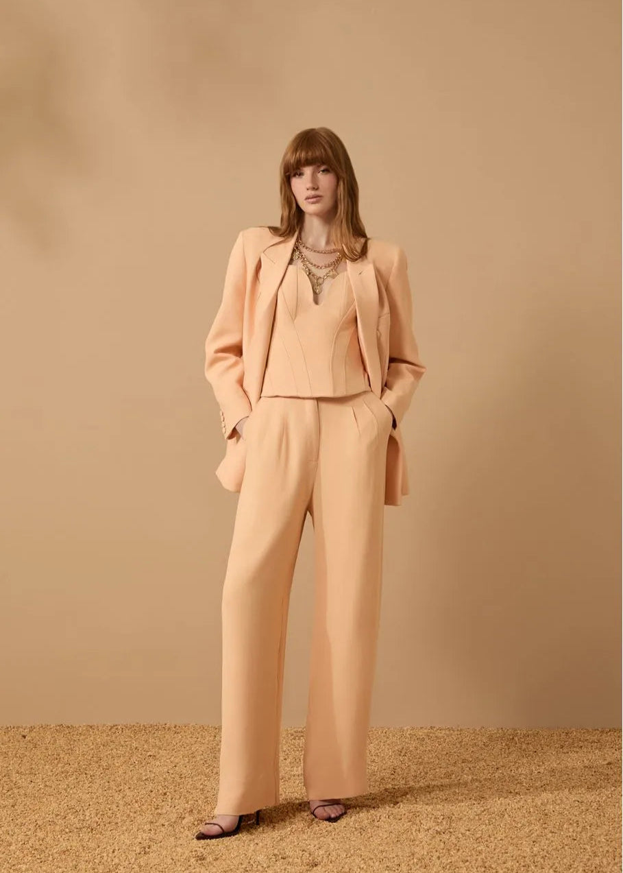 Woman wearing a peach suit standing against a beige background