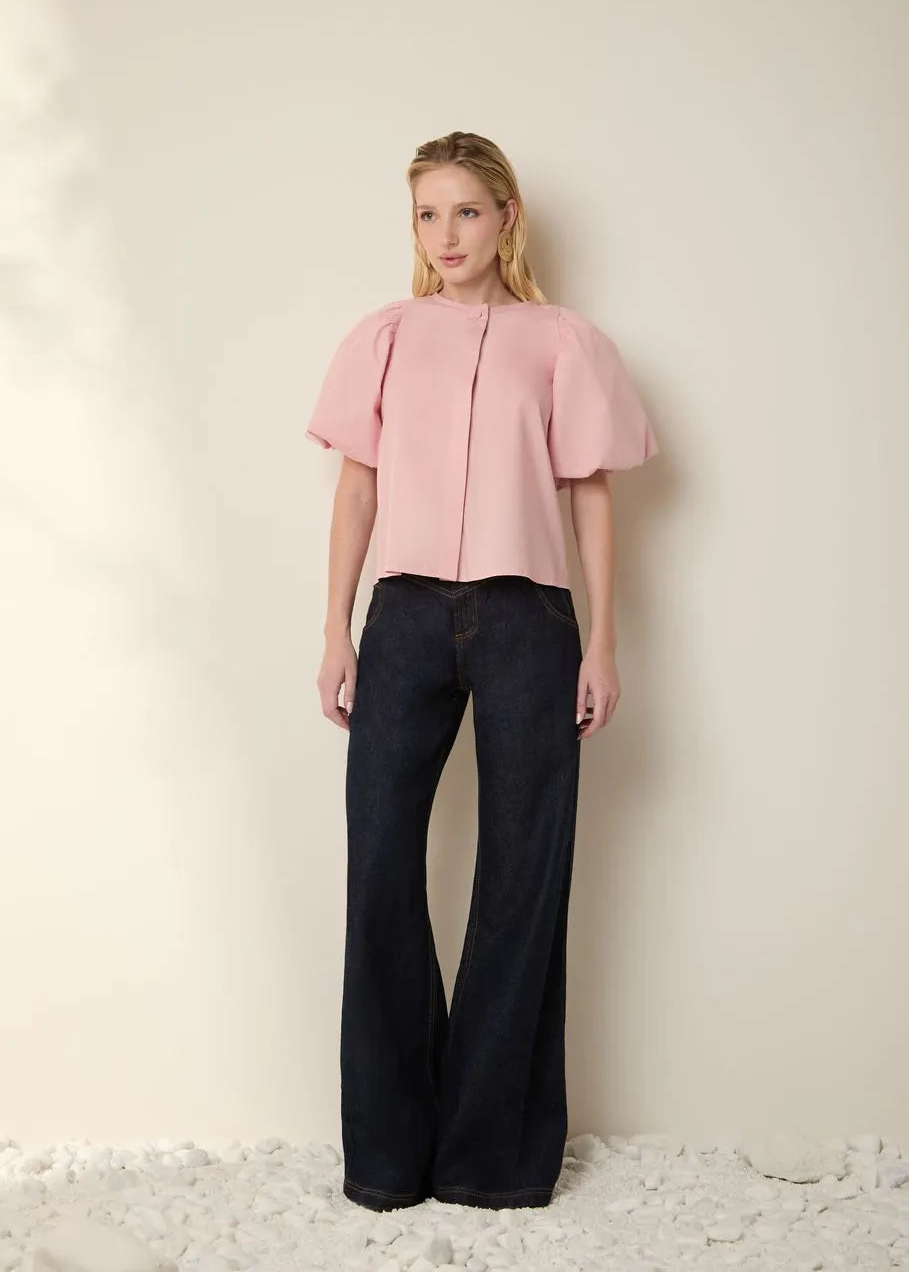 Woman wearing a pink blouse and black pants against a light background