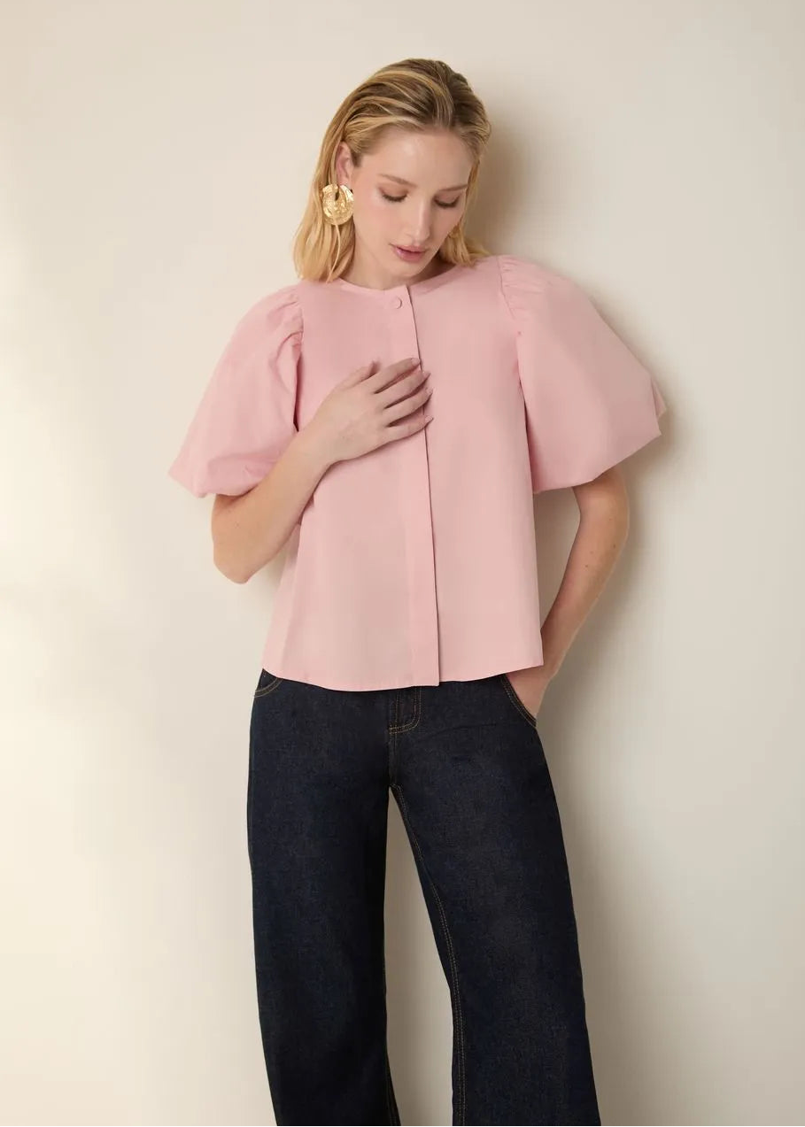 Woman wearing a pink blouse and dark jeans against a plain background