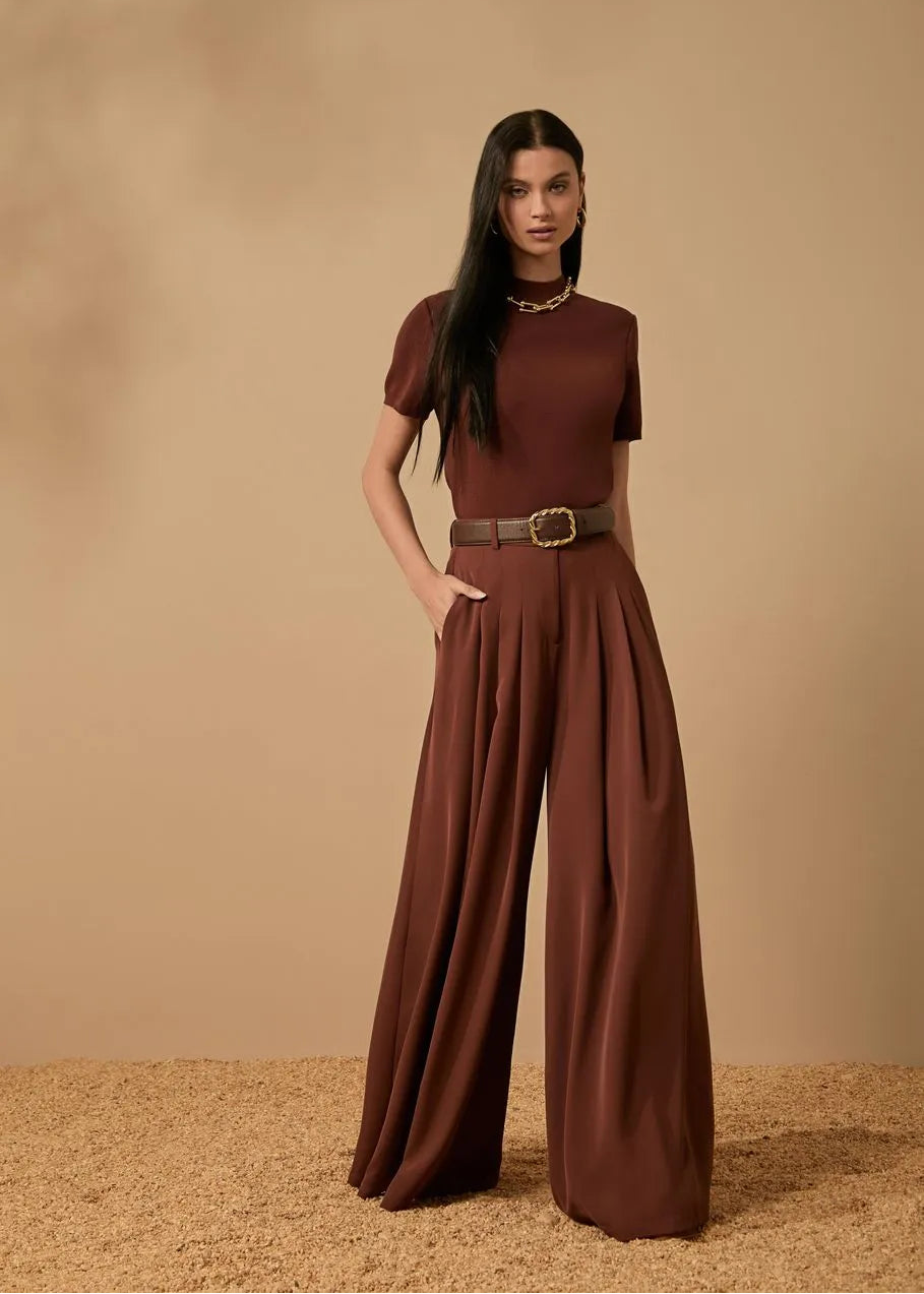 Woman wearing a brown outfit with wide-leg pants against a beige background