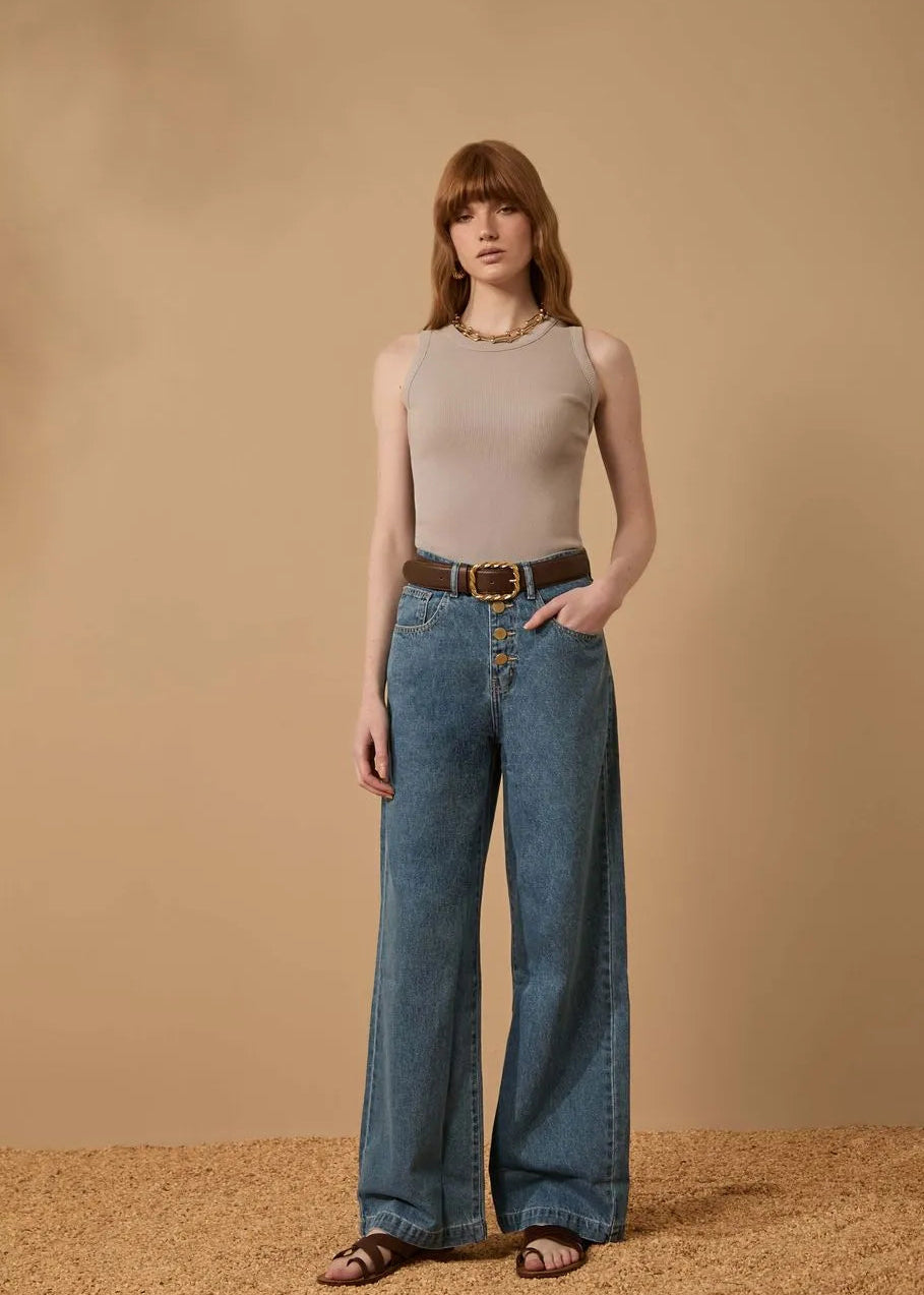 Woman wearing a beige sleeveless top and blue jeans against a beige background