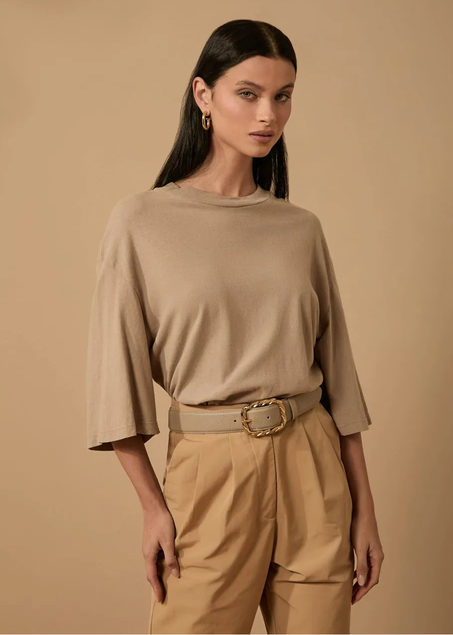 Woman wearing a beige outfit with a belt against a beige background