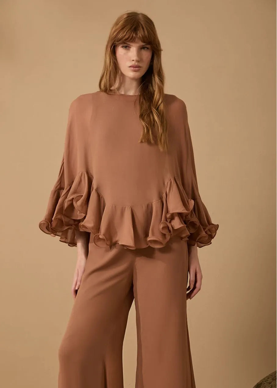 Woman wearing a brown ruffled top and pants against a beige background