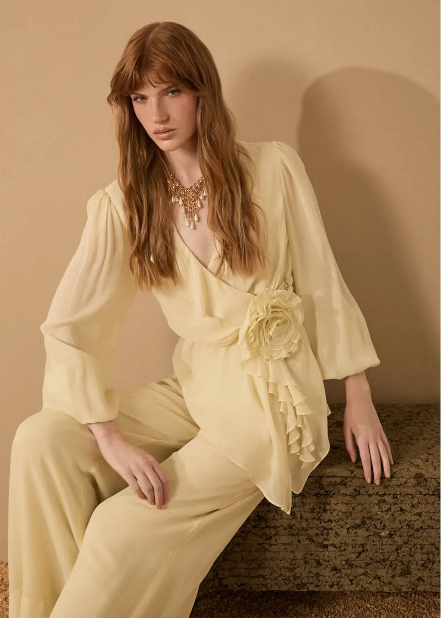 Woman in a light yellow outfit with a floral accessory against a beige background