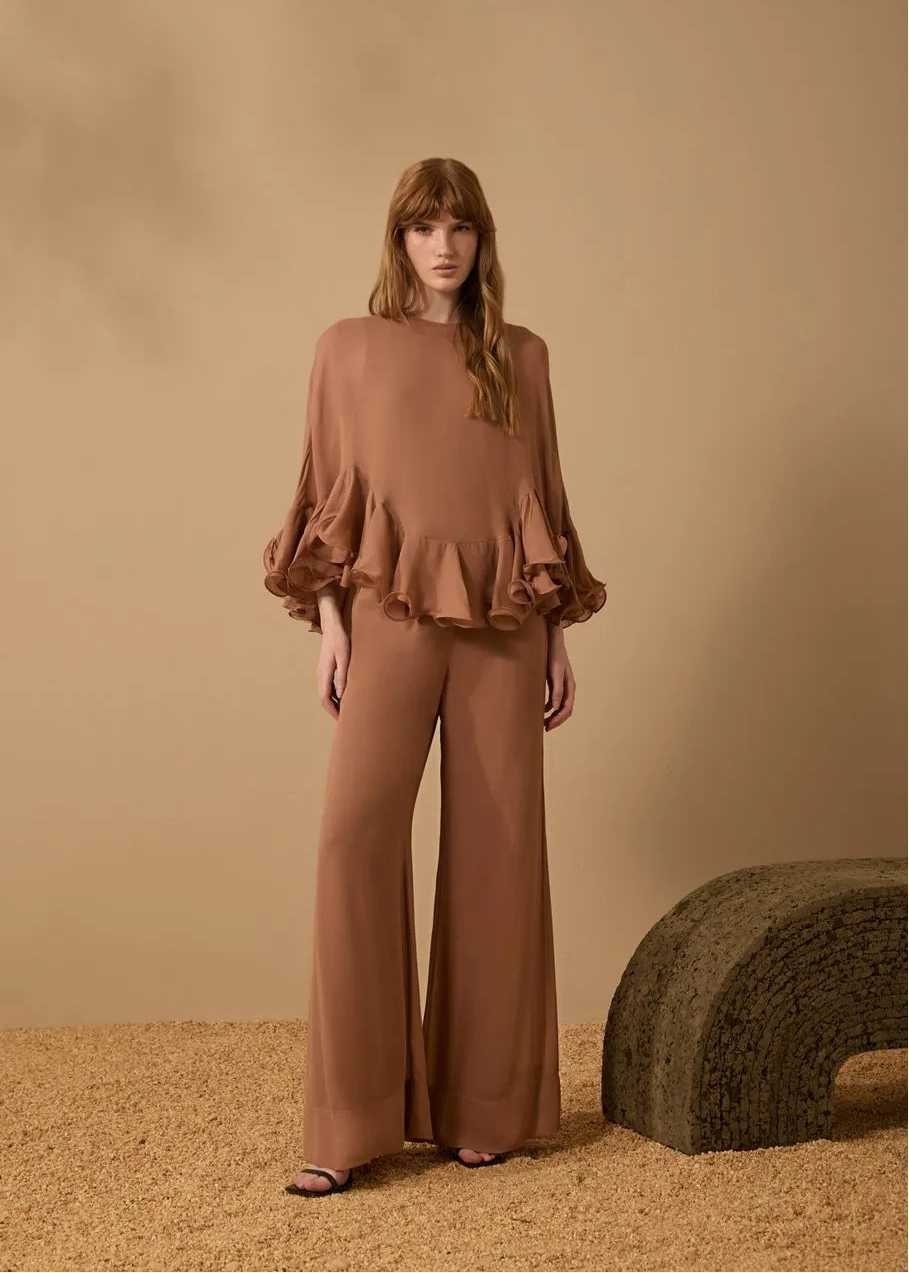 Woman wearing a brown outfit with ruffled top and wide-leg pants against a beige background