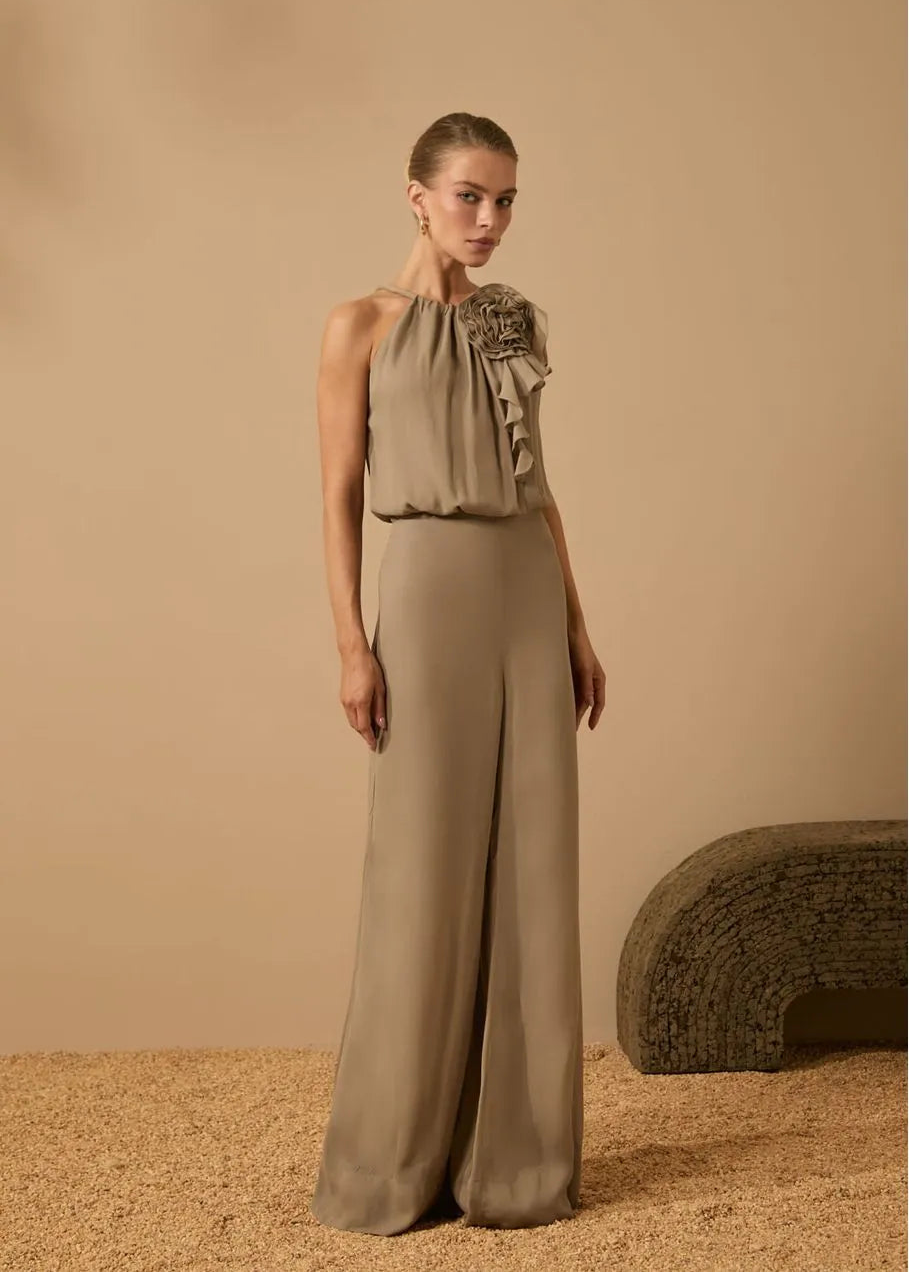 Woman wearing a beige dress with ruffled top and wide-leg pants against a beige background
