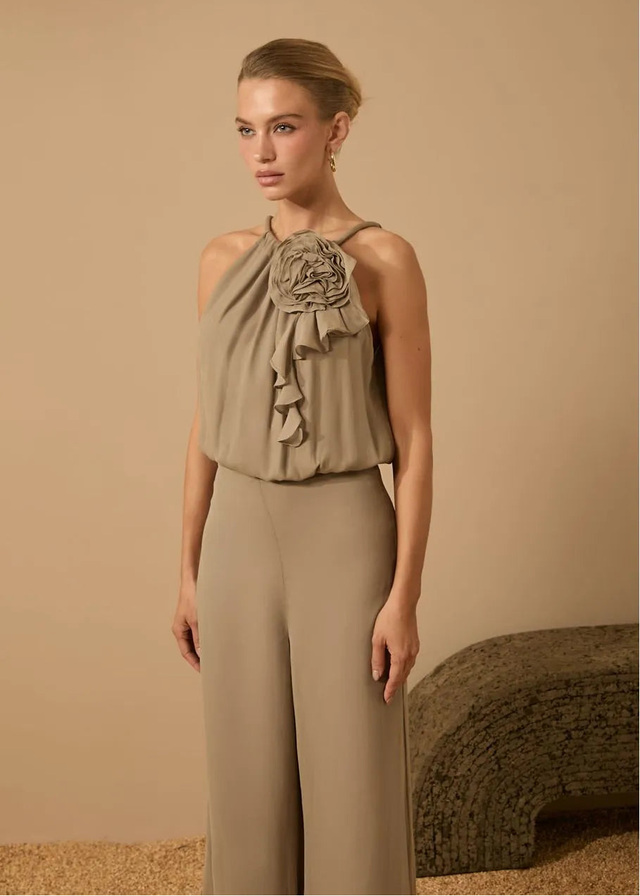 Woman wearing a beige halter top with floral details and matching pants against a beige background