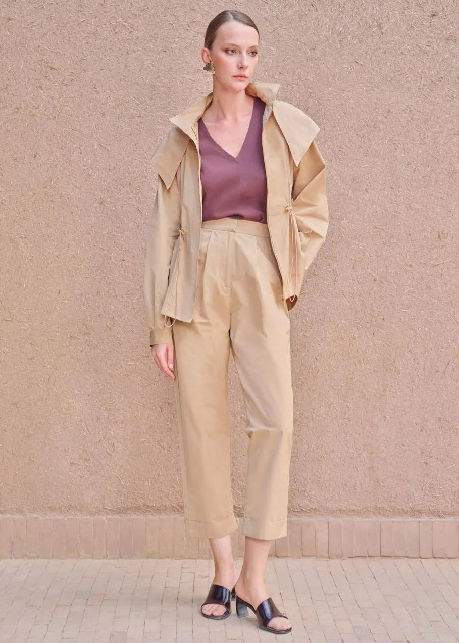 Woman wearing a beige outfit with a matching jacket and pants against a beige wall.
