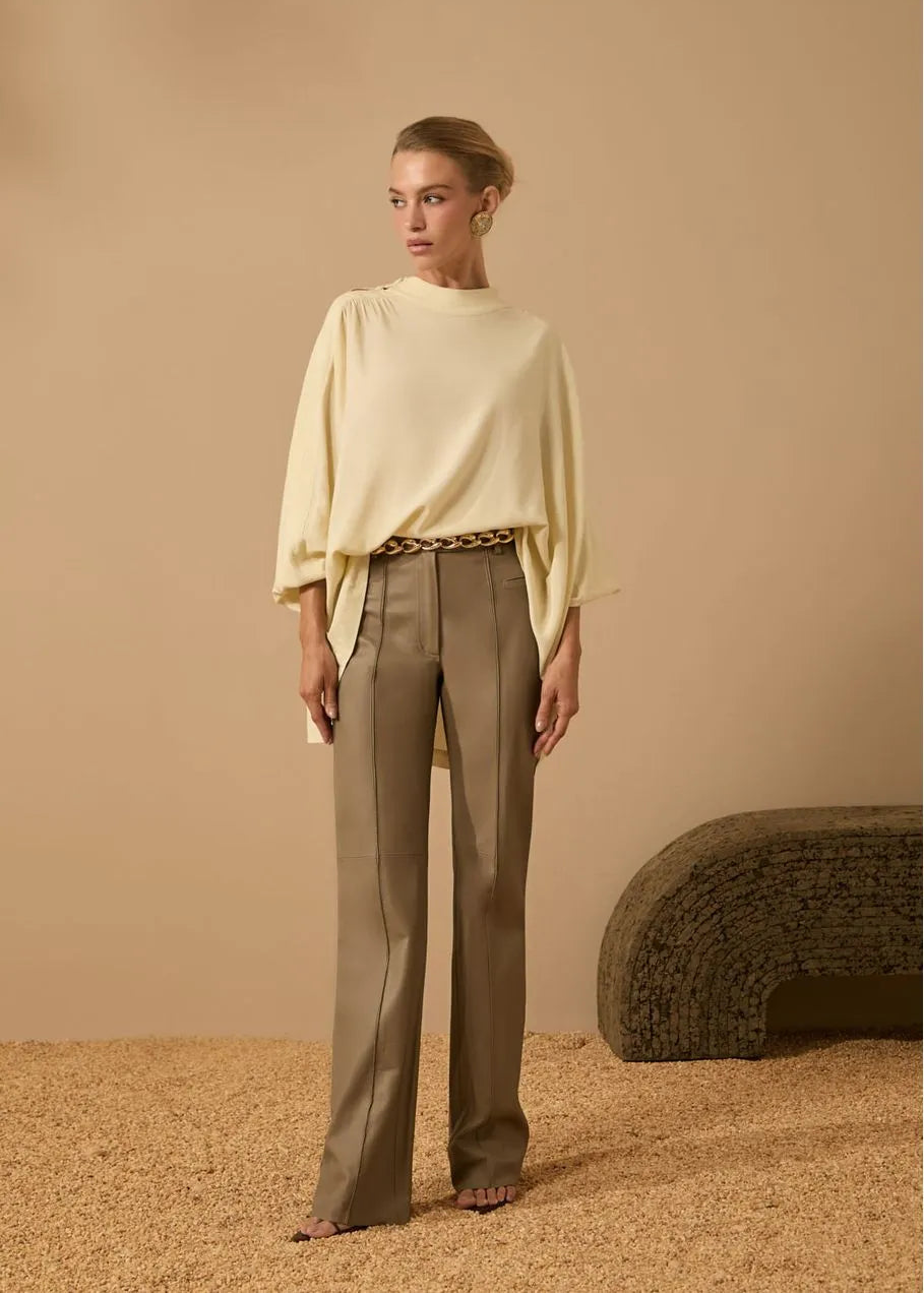Woman wearing a light yellow top and beige pants against a beige background