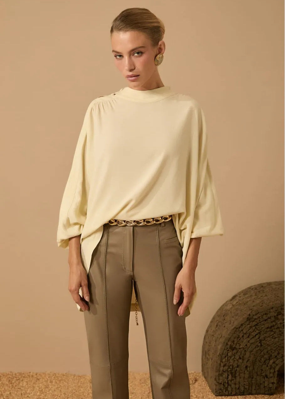 Woman wearing a light-colored blouse and beige pants against a beige background