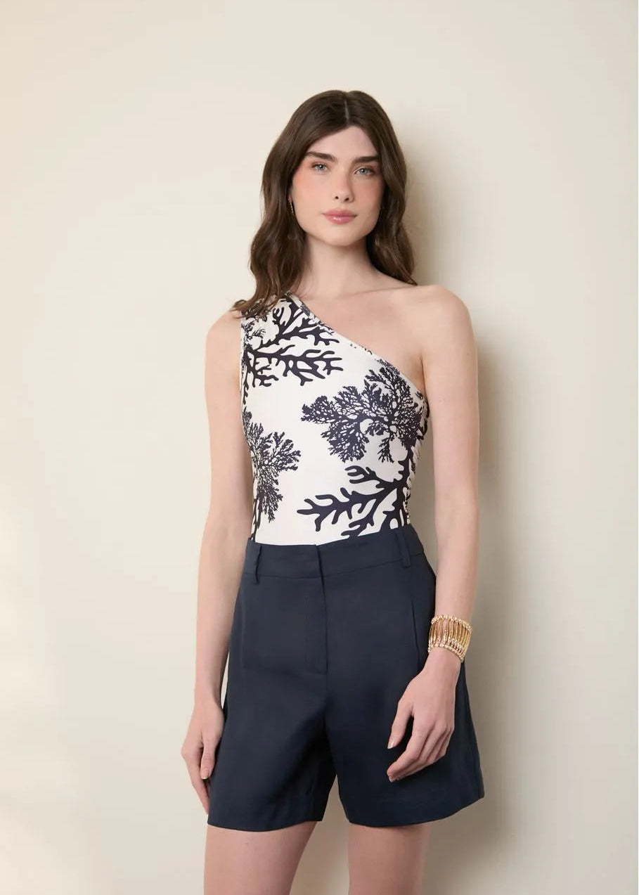 Woman wearing a one-shoulder floral top and navy shorts against a beige background