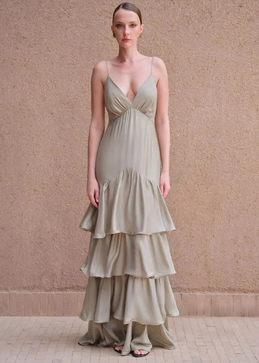 Woman wearing a flowing beige dress against a textured wall.