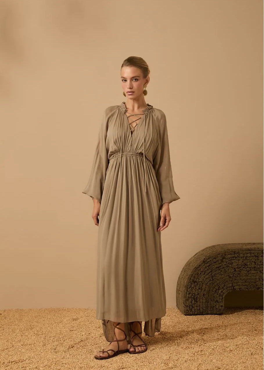 Woman wearing a long beige dress standing against a beige background