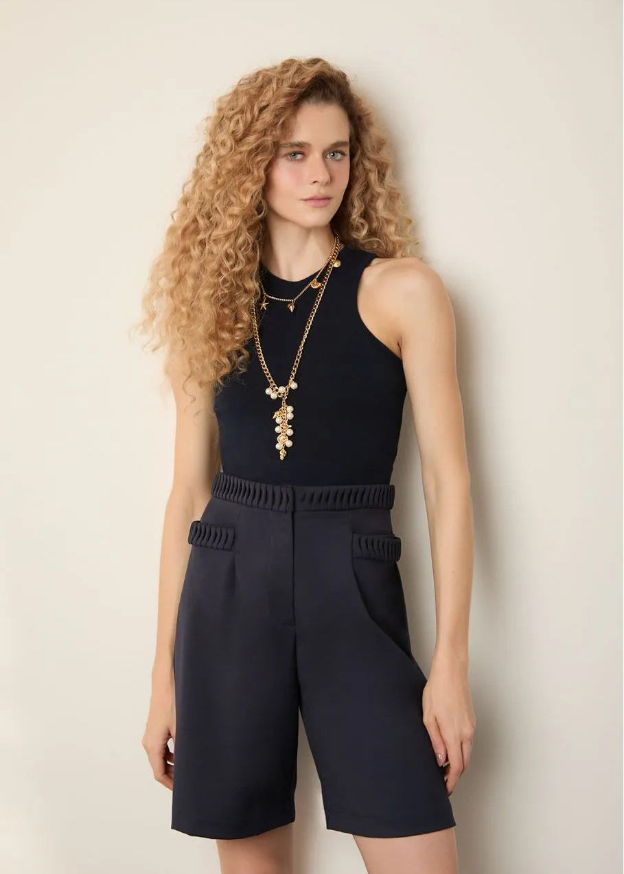 Woman wearing a black sleeveless top and navy shorts against a beige background