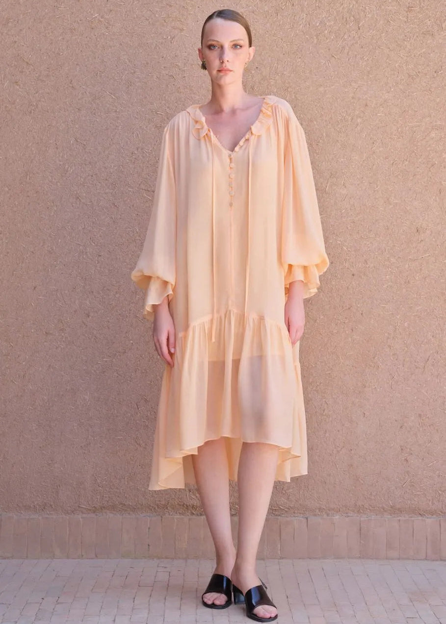 Woman wearing a light yellow dress against a beige wall.