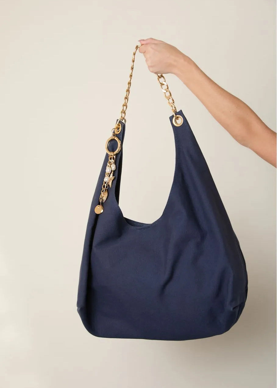 Navy blue handbag with gold chain handle held by a hand against a beige background
