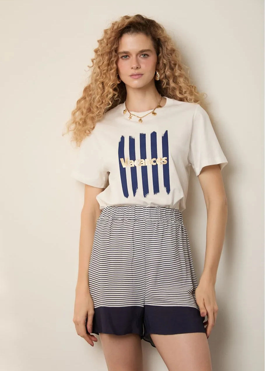 Woman wearing a white t-shirt with blue graphics and a striped skirt on a beige background