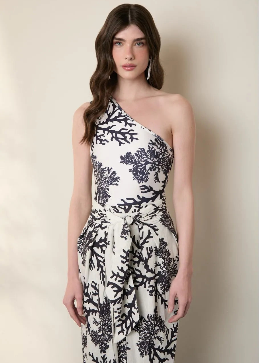 Woman wearing a one-shoulder dress with black floral pattern against a plain background