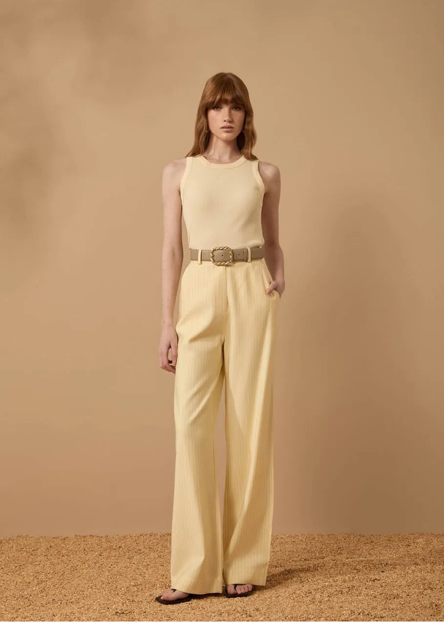 Woman wearing a light yellow sleeveless top and wide-leg pants against a beige background