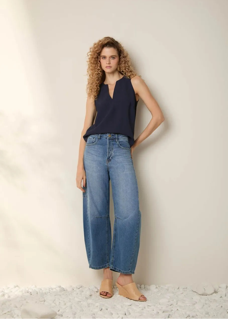 Woman wearing a navy sleeveless top and light blue jeans against a neutral background