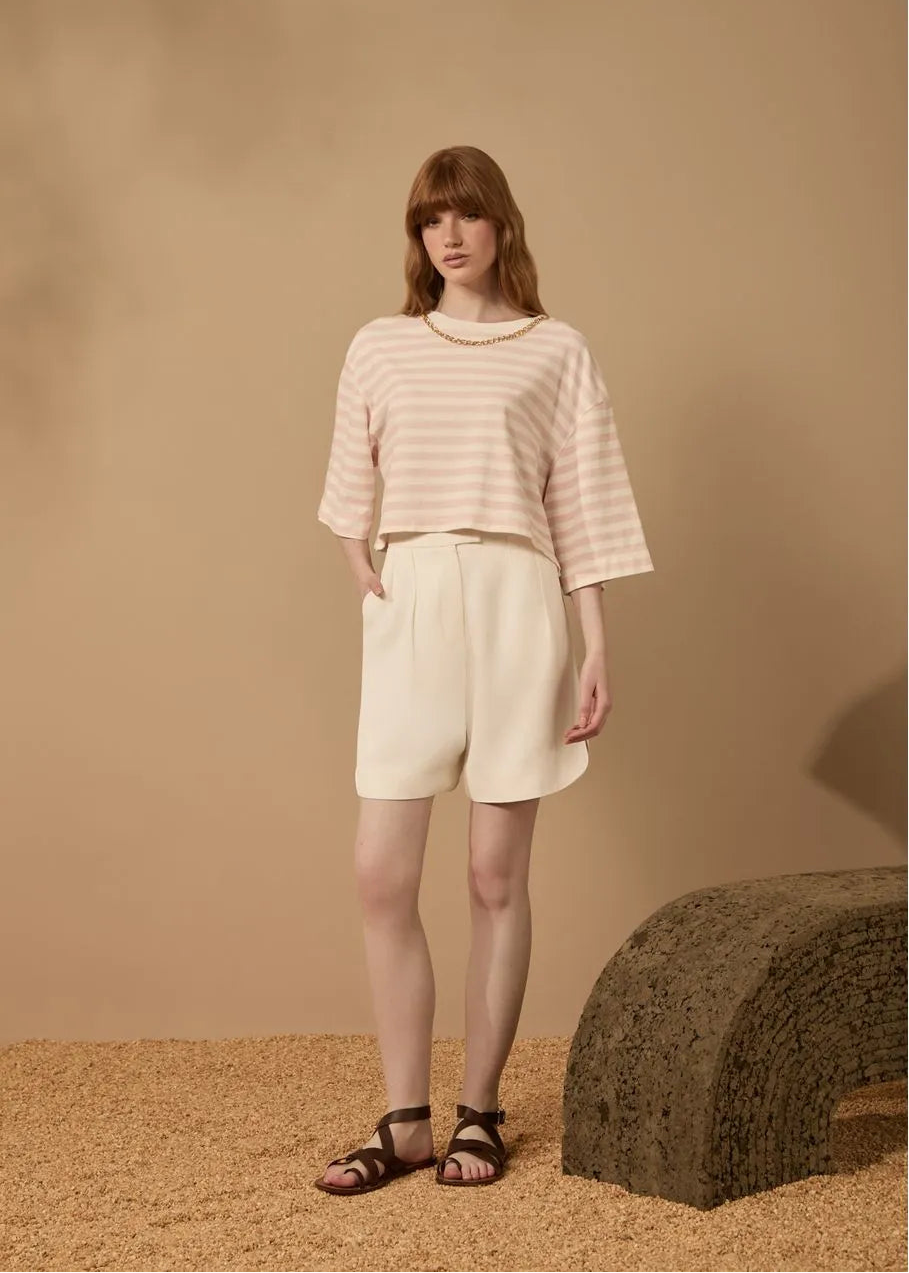 Woman wearing a striped shirt and shorts against a beige background