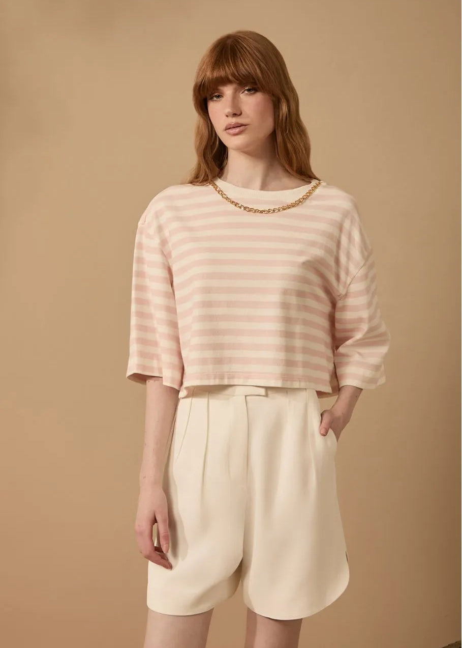 Woman wearing a striped pink and white top and beige shorts against a beige background