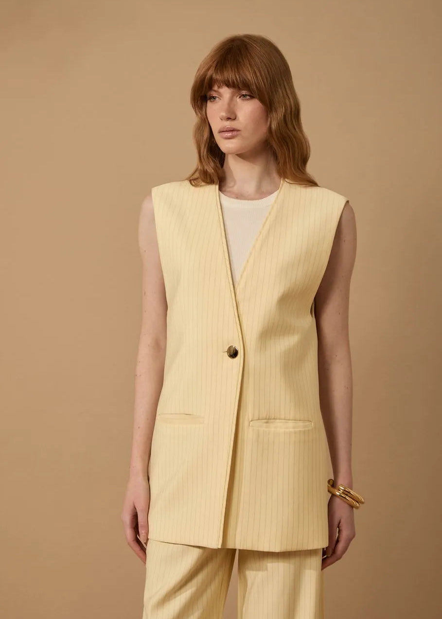 Woman wearing a light yellow vest over a white top on a beige background