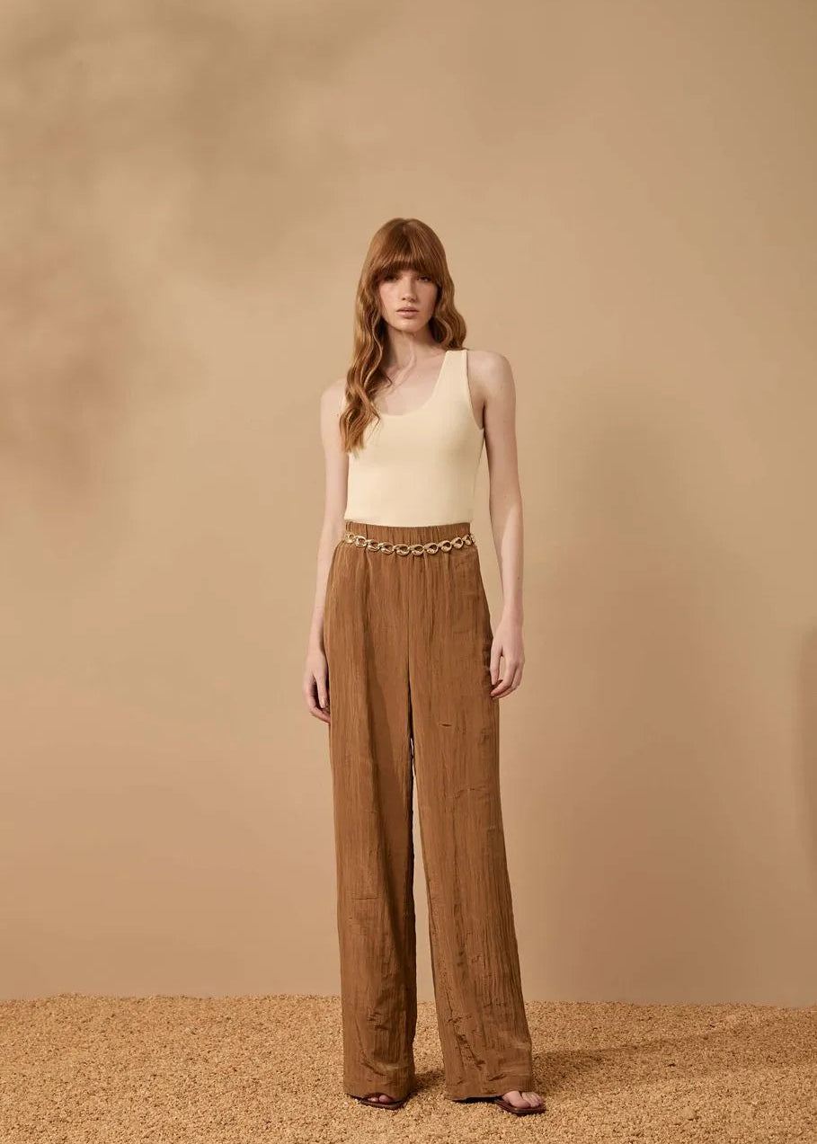 Woman wearing a beige top and brown wide-leg pants against a beige background