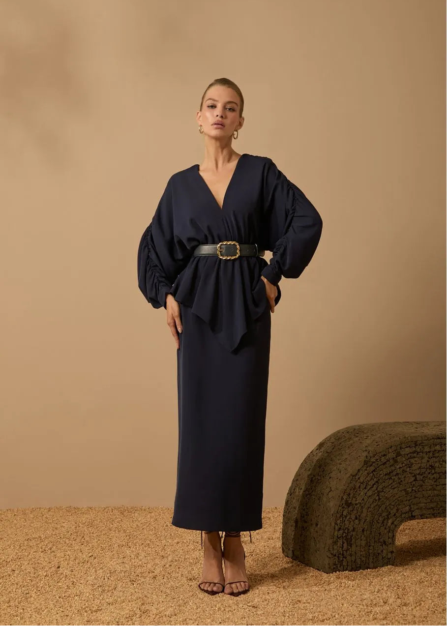 Woman wearing a navy blue dress with a belt against a beige background
