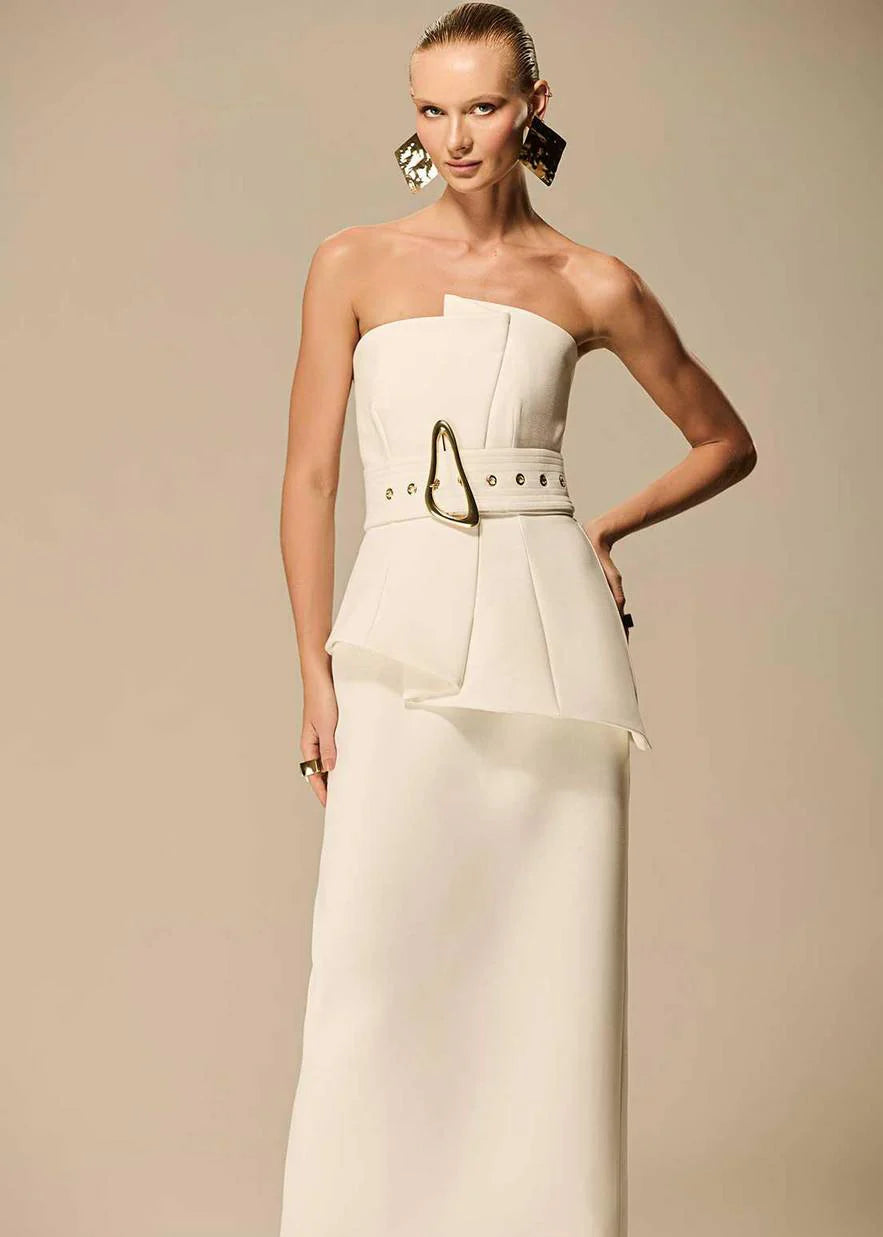 Woman wearing a strapless white gown with a gold belt against a beige background