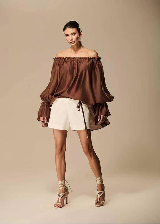 Woman wearing a brown off-shoulder top and white shorts on a beige background