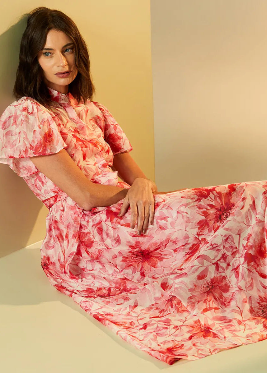 Woman wearing a red and white floral dress sitting against a beige wall.