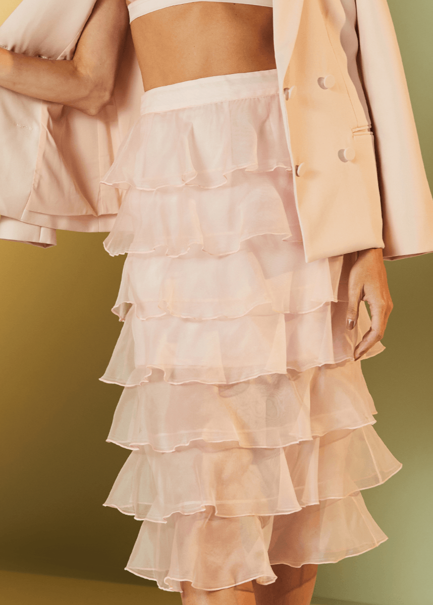 Woman wearing a light pink ruffled skirt with a matching jacket against a yellow background