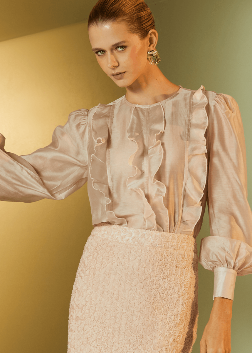 Woman wearing a light pink blouse with ruffled sleeves against a gold and green gradient background