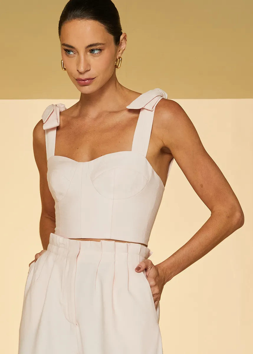 Woman wearing a white sleeveless top and pants against a beige background