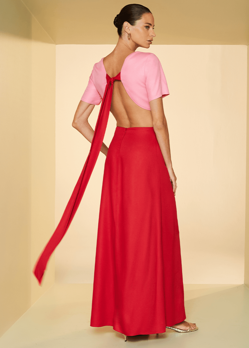 Woman wearing a pink top and red skirt with a long ribbon, standing against a plain background.