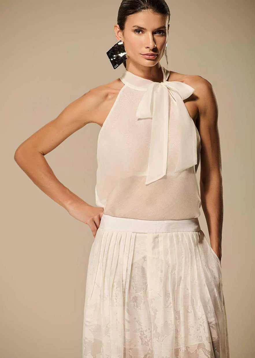 Woman wearing a white sleeveless top with a bow and a matching skirt against a beige background