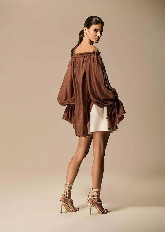 Woman wearing a brown off-shoulder top and white shorts on a beige background
